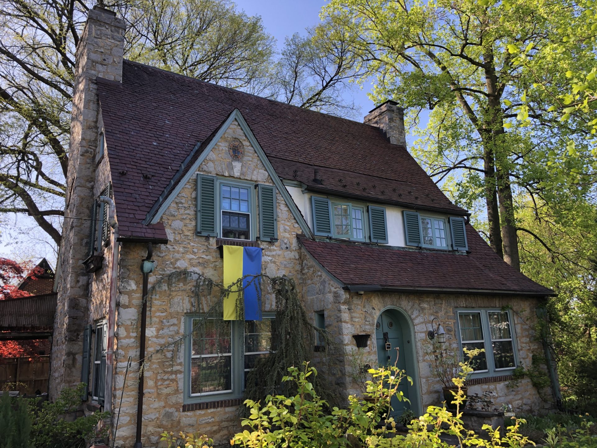 stone house with green door and shutters and Ukrainian flag hanging from a window