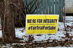 A yellow yard sign with black letters reads "We're For Integrity" / #FairTrialForSubu